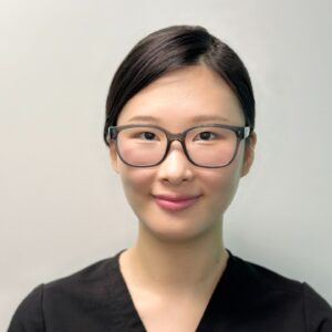 A headshot of Dr. Jennifer Jung in front of a white background. She wears black scrubs and glasses.